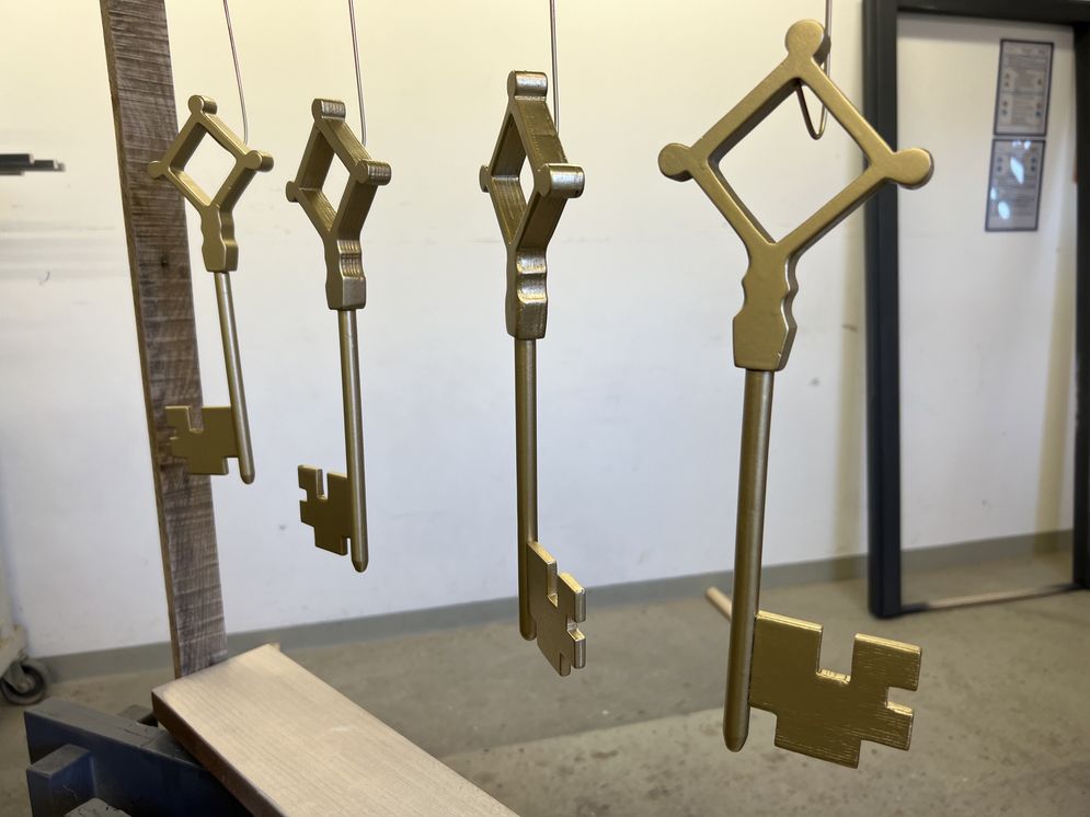 Das Foto zeigt vier golden lackierte Schlüssel die auf einem Ständer trocknen