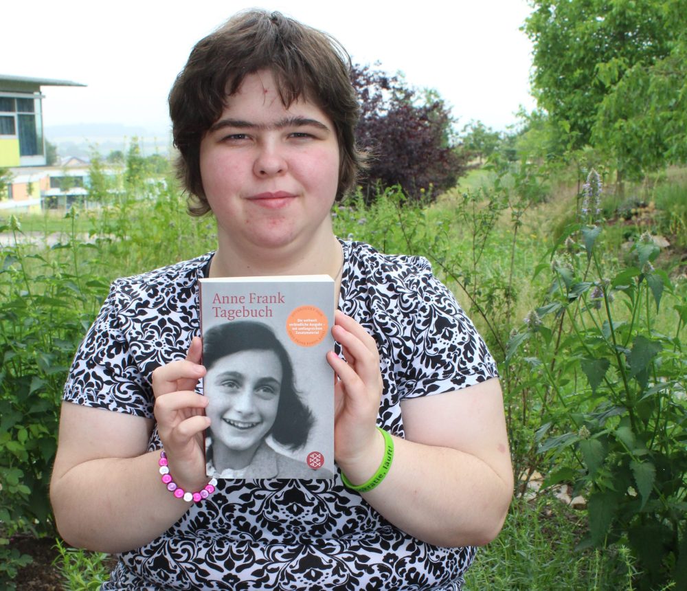 Unsere Auszubildende Laura-Jannina mit dem Anne Frank Tagebuch und dem Armband "Demokratie, läuft"