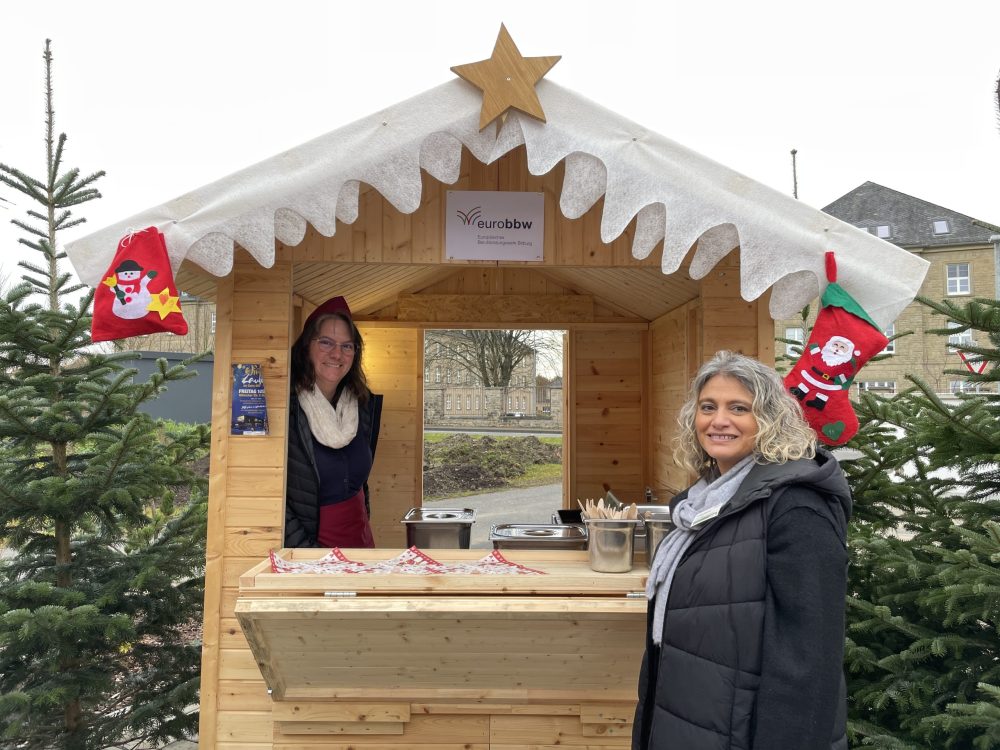 Eine Person in und eine vor einer weihnachtlich geschmückten Holzbude