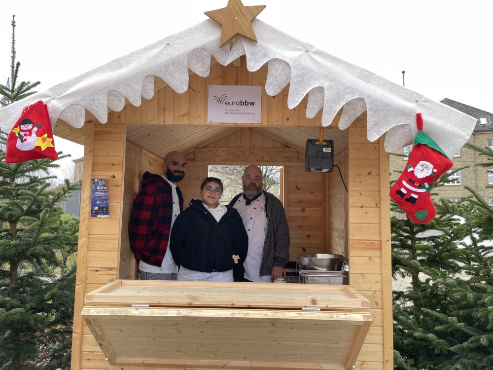 Drei Personen in einer weihnachtlich geschmückten Holzbude
