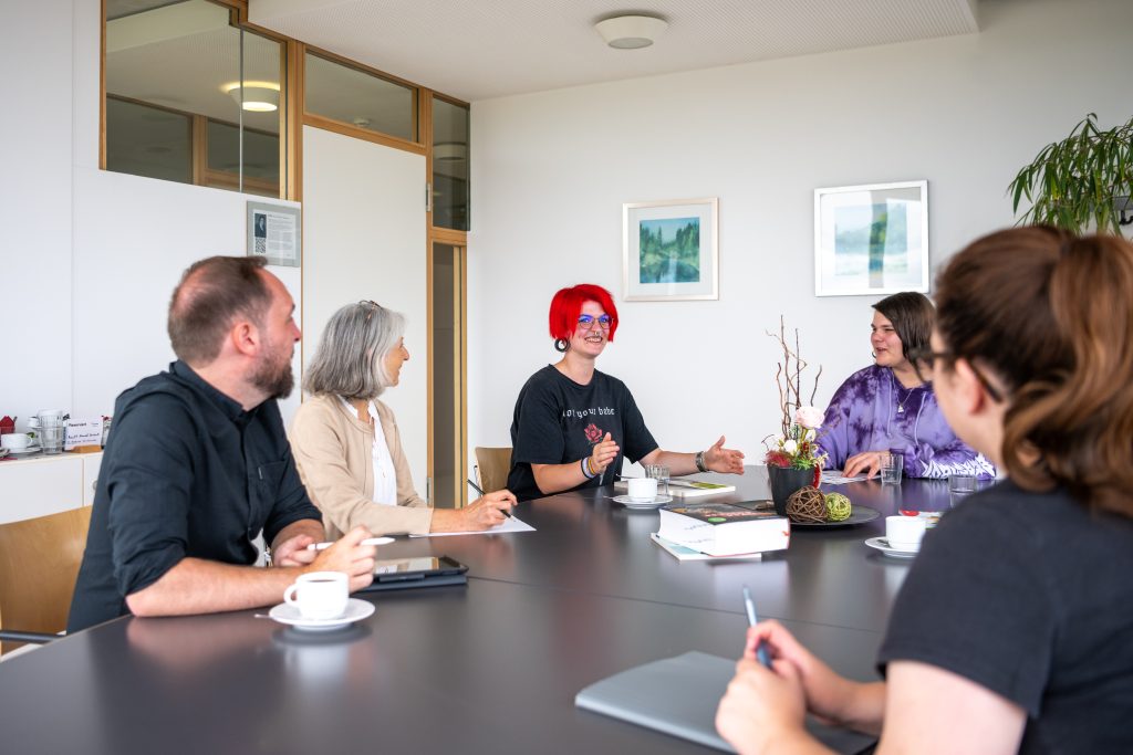 Fünf Personen sitzen um einen Tisch und führen ein Gespräch