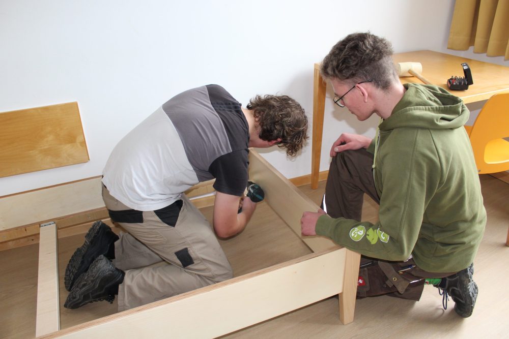 zwei Auszubildende verschrauben einen Bettrahmen