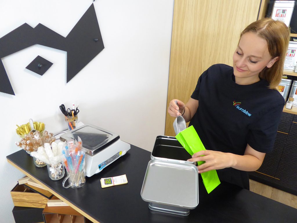 eine junge Frau füllt Tee aus einer Dose in eine Teetüte