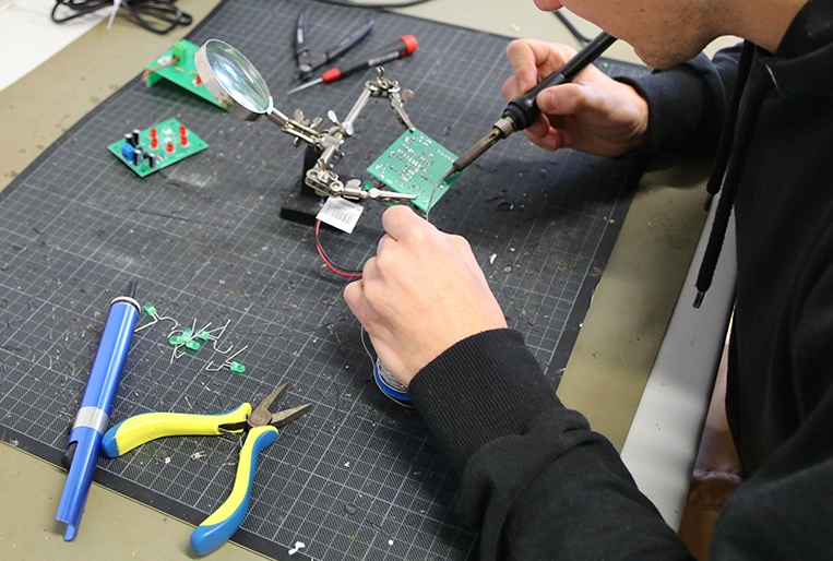 man sieht eine Person, die mit einem Lötkolben eine Platine bearbeitet