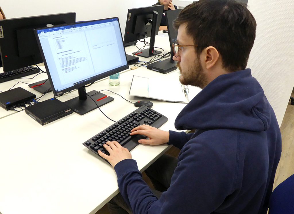 ein junger Mann sitzt vor einem Bildschirm und arbeitet
