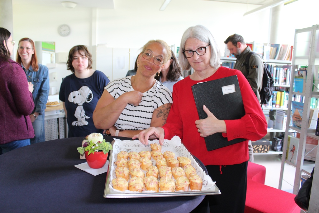 Besucher*innen beim Stöbern in der Mediathek und Probieren der Häppchen