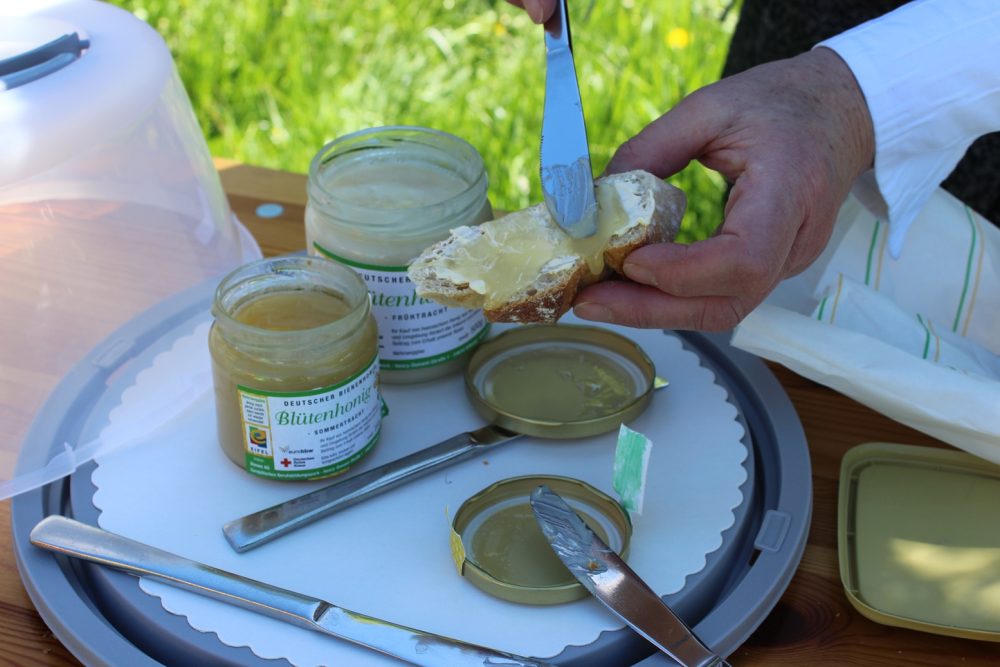 man sieht eine Hand, die mit einem Messer Honig auf eine Scheibe Brot streicht