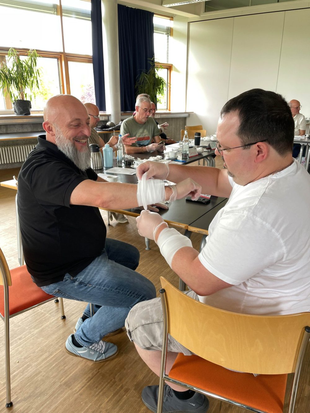 ein Kollege legt bei einem anderen Kollegen einen Verband am Unterarm an