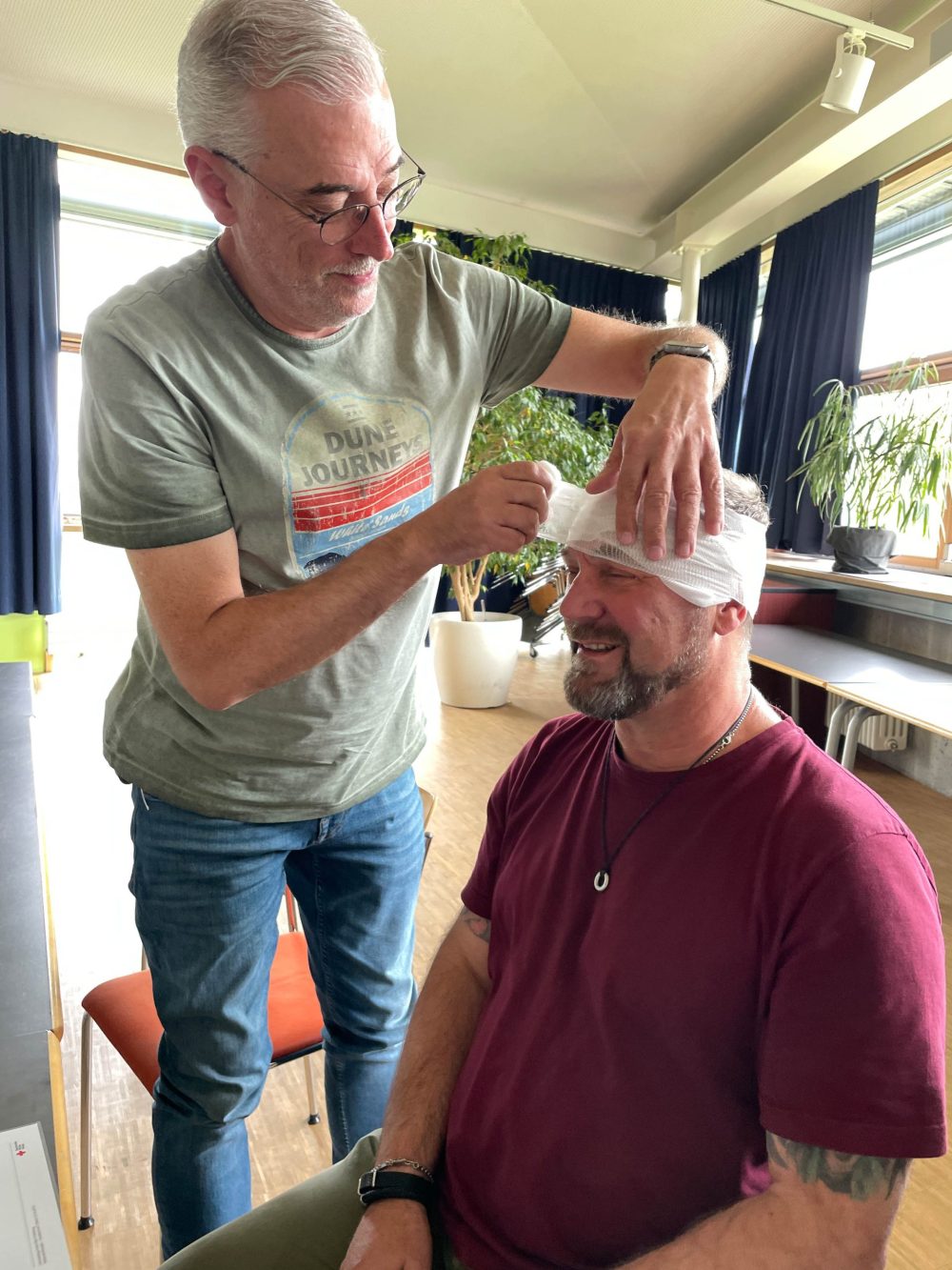 ein Kollege legt bei einem anderen Kollegen einen Verband am Kopf an