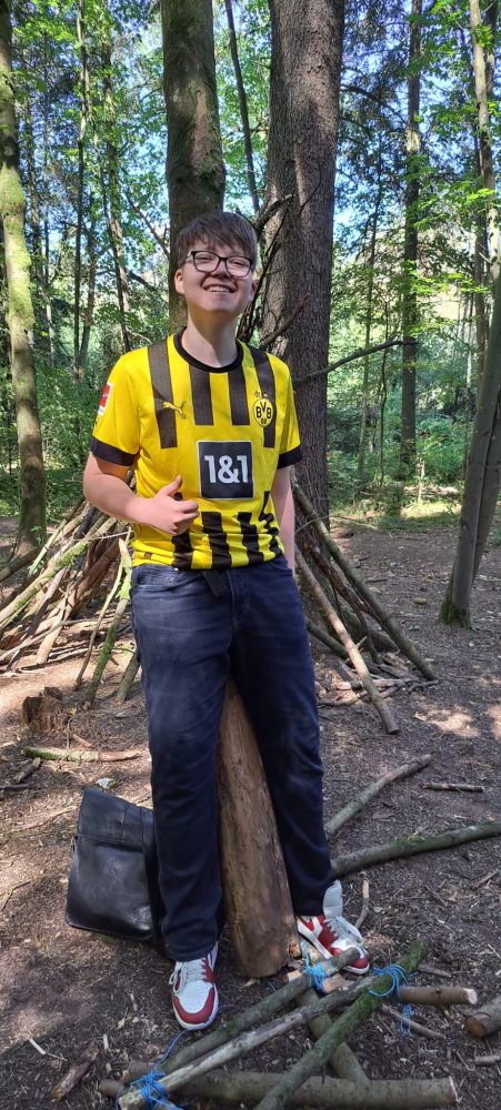 Ein Teilnehmender sitzt auf einem Baumstamm