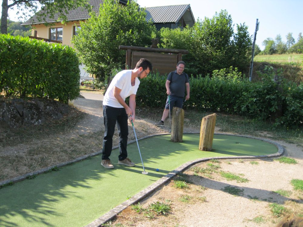 Zwei Personen auf einer Minigolfanlage; einer schlägt gerade