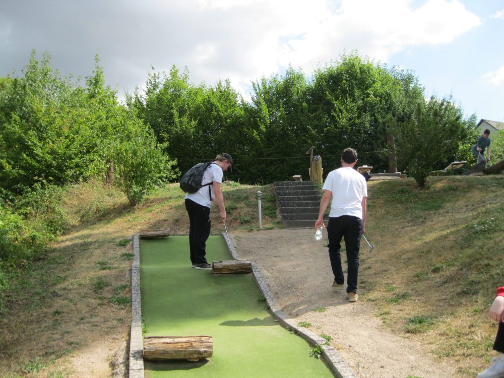 Zwei Personen auf einer Minigolfanlage; einer schlägt gerade