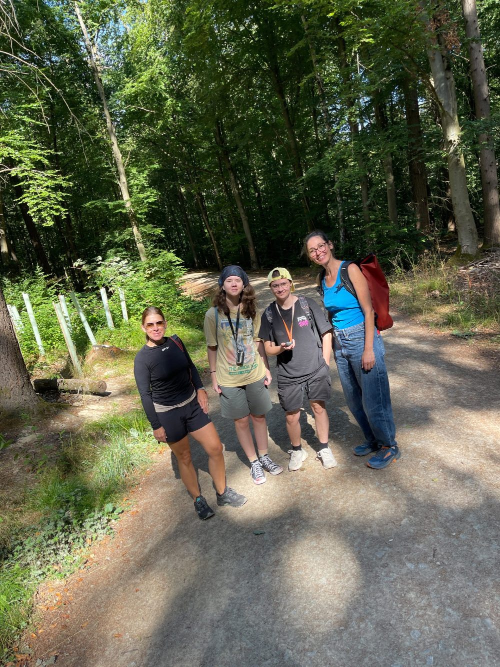 vier Personen stehen auf einem Waldweg und blicken in die Kamera