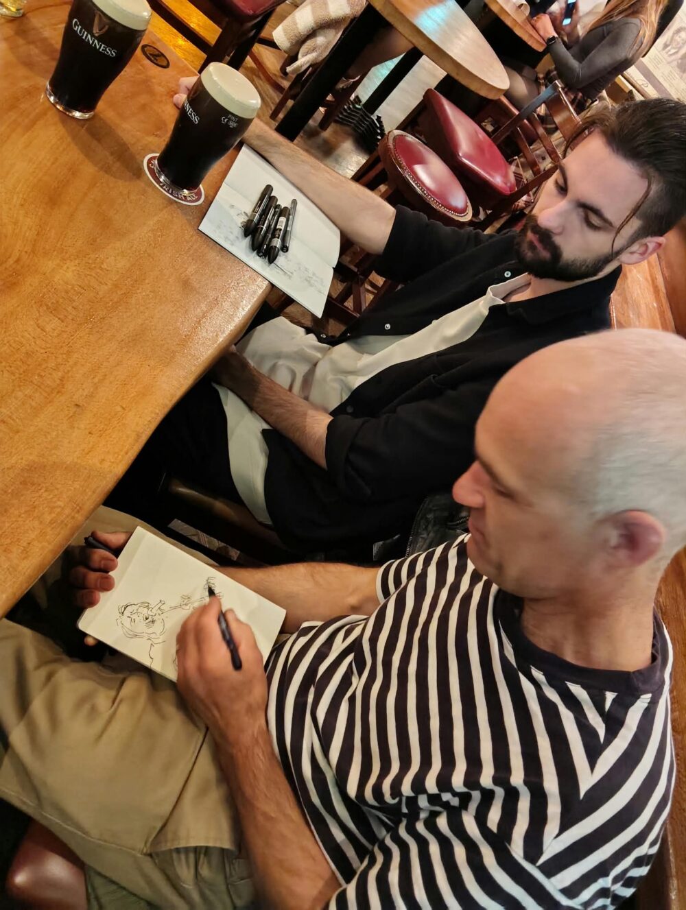 zwei Personen sitzen im Pub und zeichnen in ihre Skizzenbücher