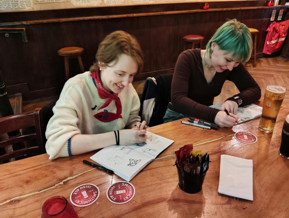 zwei Personen sitzen im Pub und zeichnen in ihre Skizzenbücher